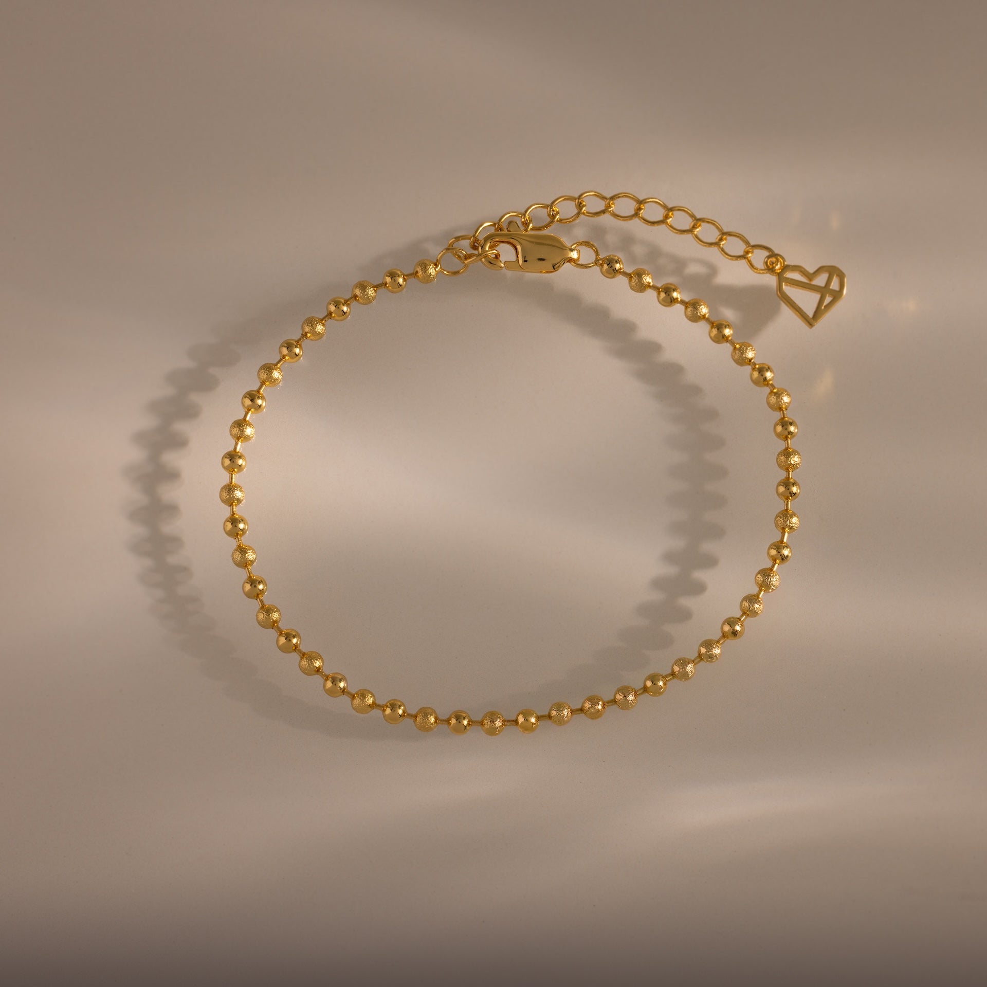 Dune Beaded Bracelet in 18K Gold features polished beads, an adjustable chain, and a heart charm, displayed on a neutral background.