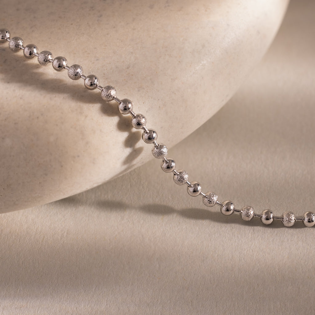 Close-up of the Dune Beaded Bracelet in Silver draped across a smooth, light stone surface, showcasing its polished silver beads.