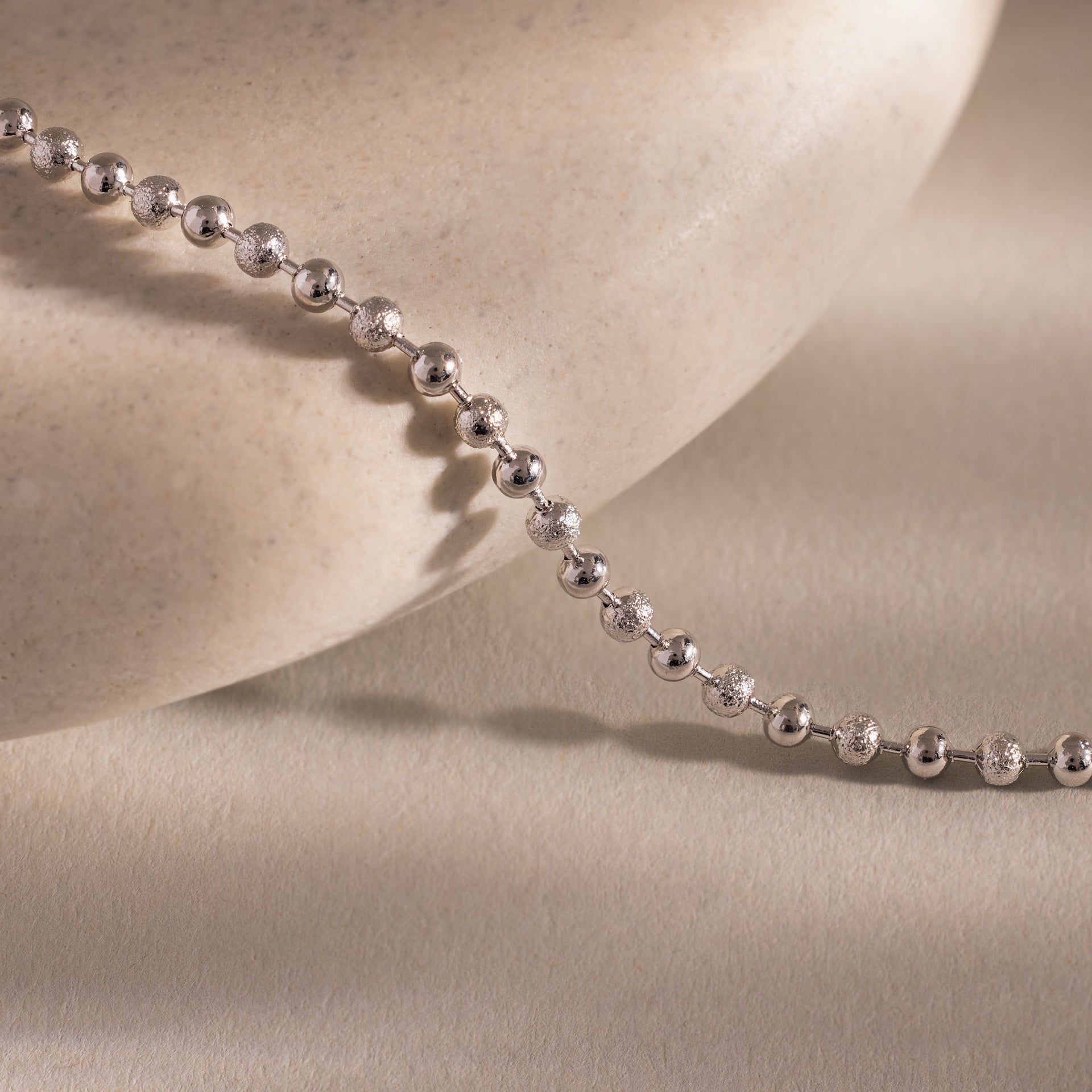 Close-up of the Dune Beaded Bracelet with polished silver beads resting on a smooth, beige stone surface.