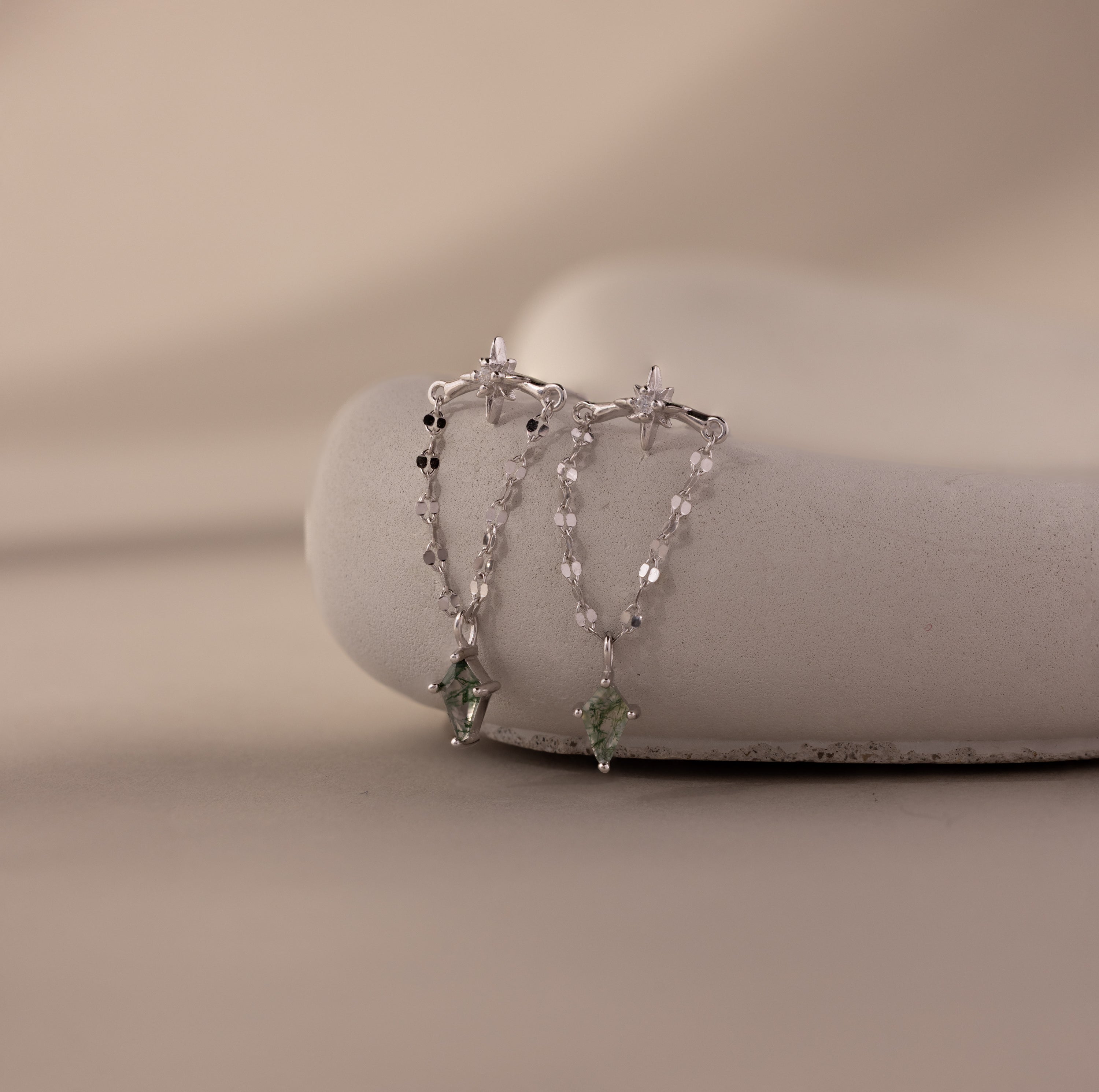 Agate Star Chain Earrings in Sterling Silver feature delicate chains and green agate star charms, displayed on a smooth stone—celestial earrings perfect for adding a whimsical touch.