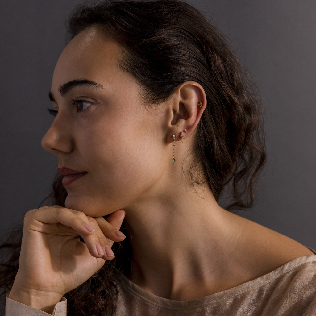 A woman with wavy brown hair looks to the side, resting her chin on her hand, wearing modern essential jewelry and Agate Diamond Dangle Earrings.