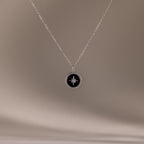 The Onyx Star Pendant Necklace in Sterling Silver features a round black onyx with a celestial star design, shown against a soft beige background.