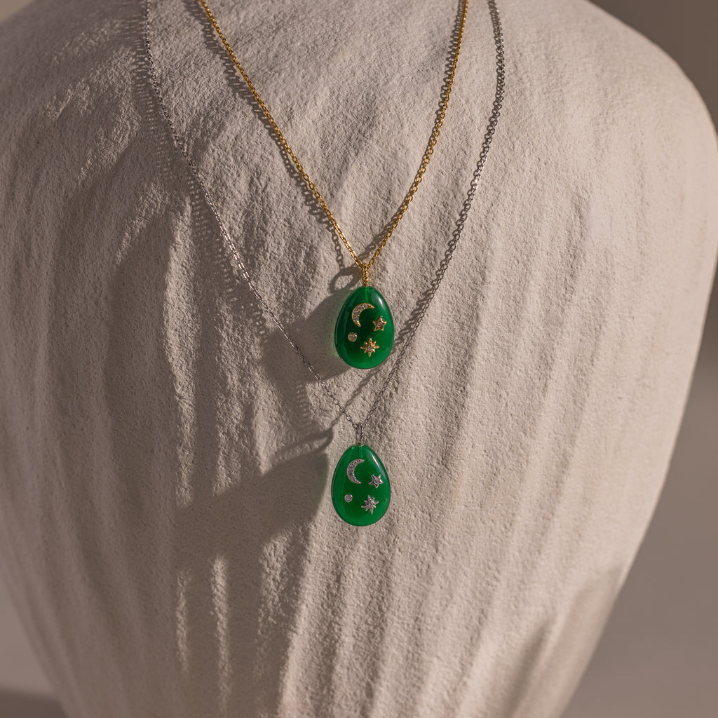 The Celestial Gemstone Pendant Necklace, featuring green gemstones on gold and silver chains, adds celestial elegance to your Moon and Stars Jewelry collection. Both are beautifully displayed on a fabric bust.