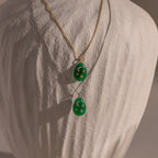 The Celestial Gemstone Pendant Necklace, featuring green gemstones on gold and silver chains, adds celestial elegance to your Moon and Stars Jewelry collection. Both are beautifully displayed on a fabric bust.