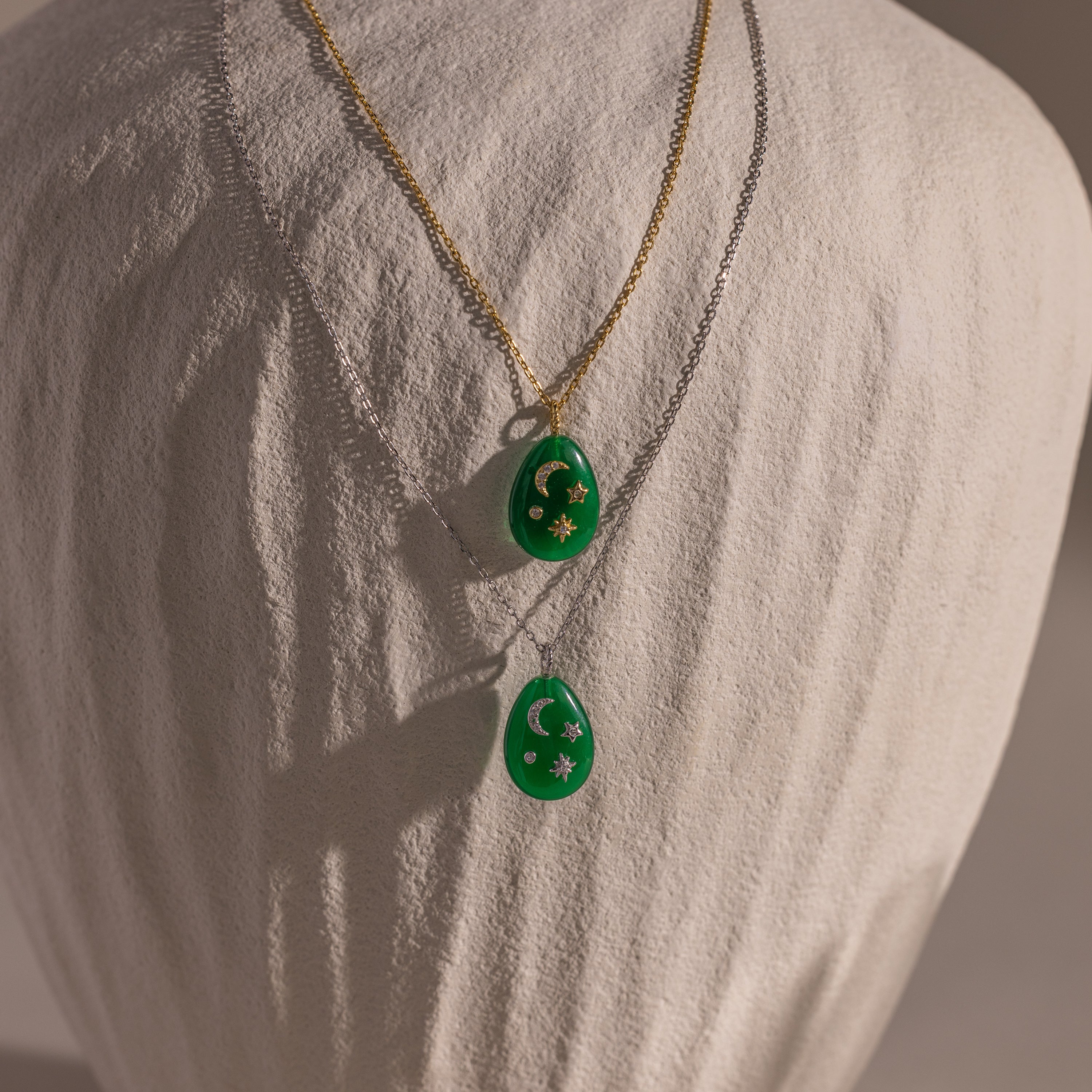 The Celestial Gemstone Pendant Necklace, featuring green gemstones on gold and silver chains, adds celestial elegance to your Moon and Stars Jewelry collection. Both are beautifully displayed on a fabric bust.