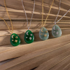 Four Celestial Gemstone Pendant Necklaces with moon and star designs, featuring gold and silver chains and a standout green gemstone piece, are beautifully displayed on a wooden surface.