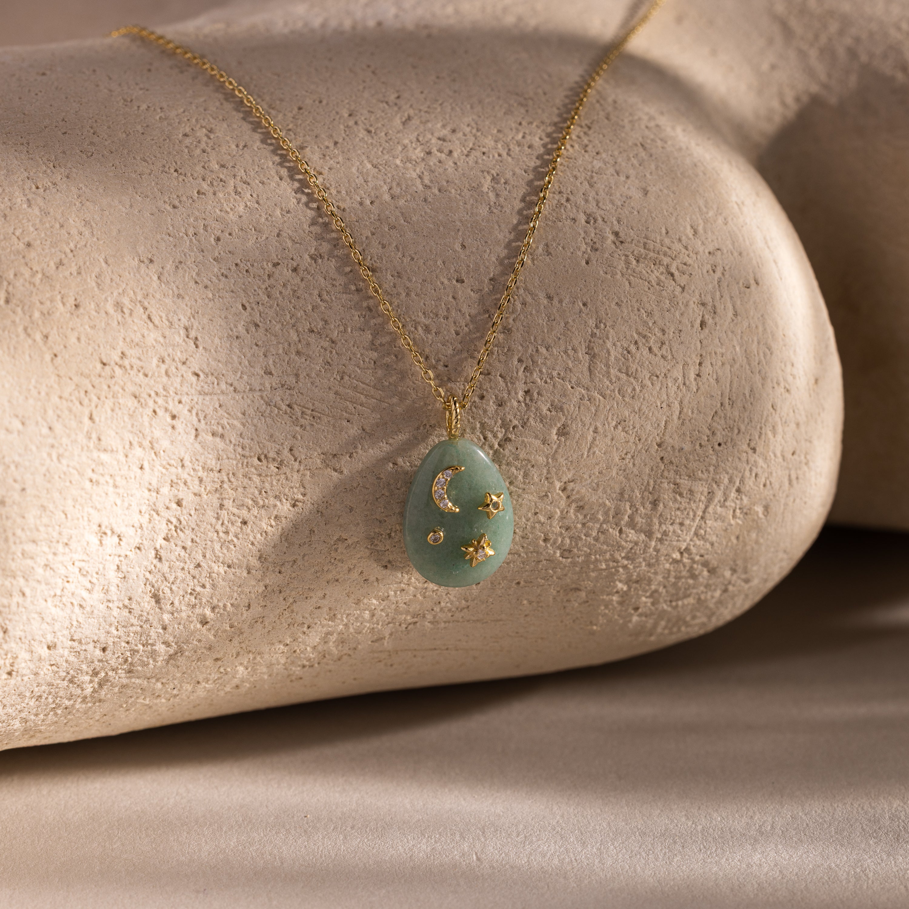 Celestial Aventurine Pendant Necklace with a green aventurine oval pendant, crescent moon and star charms, shown on a stone background.