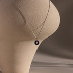 The Onyx Star Pendant Necklace in Sterling Silver is draped over a textured beige abstract sculpture, set against a neutral background.