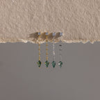 Four Agate Diamond Dangle Earrings with green gemstones in gold and silver, displayed on textured beige fabric—showcasing modern essential jewelry.
