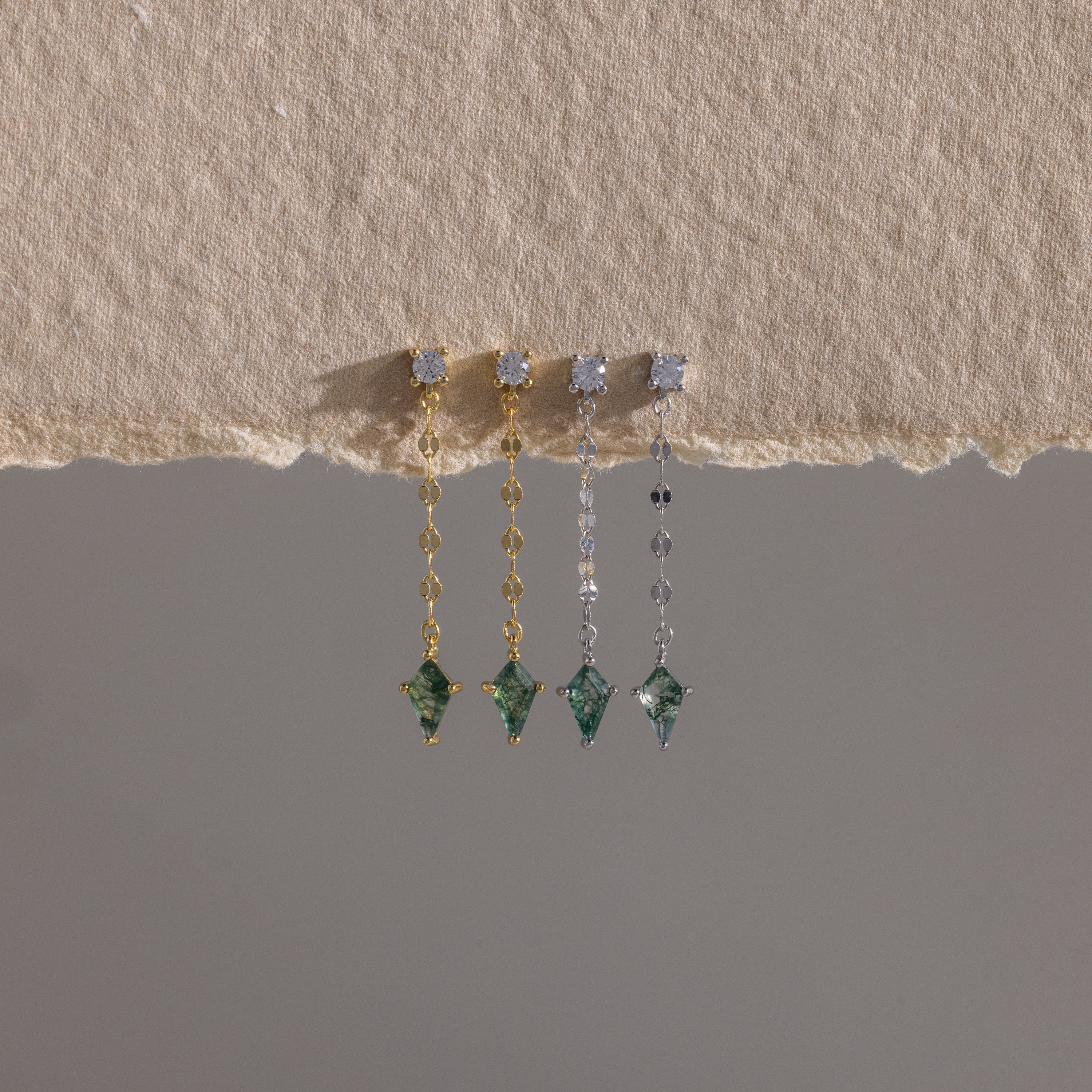 Four Agate Diamond Dangle Earrings with green gemstones in gold and silver, displayed on textured beige fabric—showcasing modern essential jewelry.
