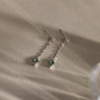 Agate Diamond Dangle Earrings with clear stones and green gemstone ends lie on a textured beige surface—a modern essential jewelry piece.