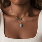 Close-up of a woman wearing two gold necklaces with green stone pendants, including the Celestial Gemstone Pendant Necklace, over a cream ribbed top.