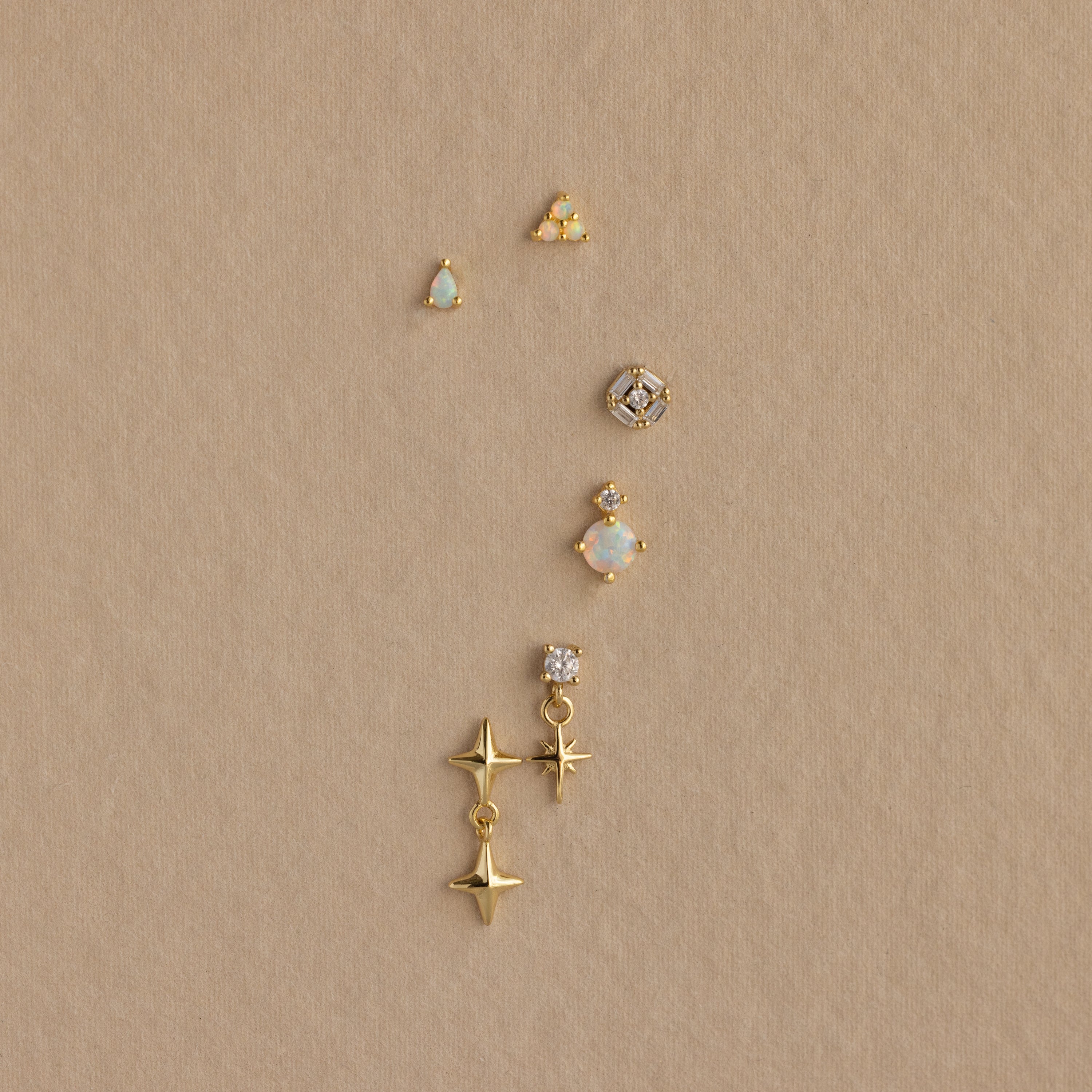 Six 18K gold Opal Cluster Flatback Studs with opal and star designs, arranged vertically on a textured beige background—perfect for an iridescent opals-inspired ear stack.