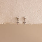 A straight-on product display of the 18k silver Diamond Star Flatback Earrings against a soft beige and off-white background, highlighting the charm's clean symmetry.
