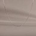 The Dainty Herringbone Necklace in Sterling Silver is displayed on a neutral beige background, ideal for adding a subtle shine to your layered look.