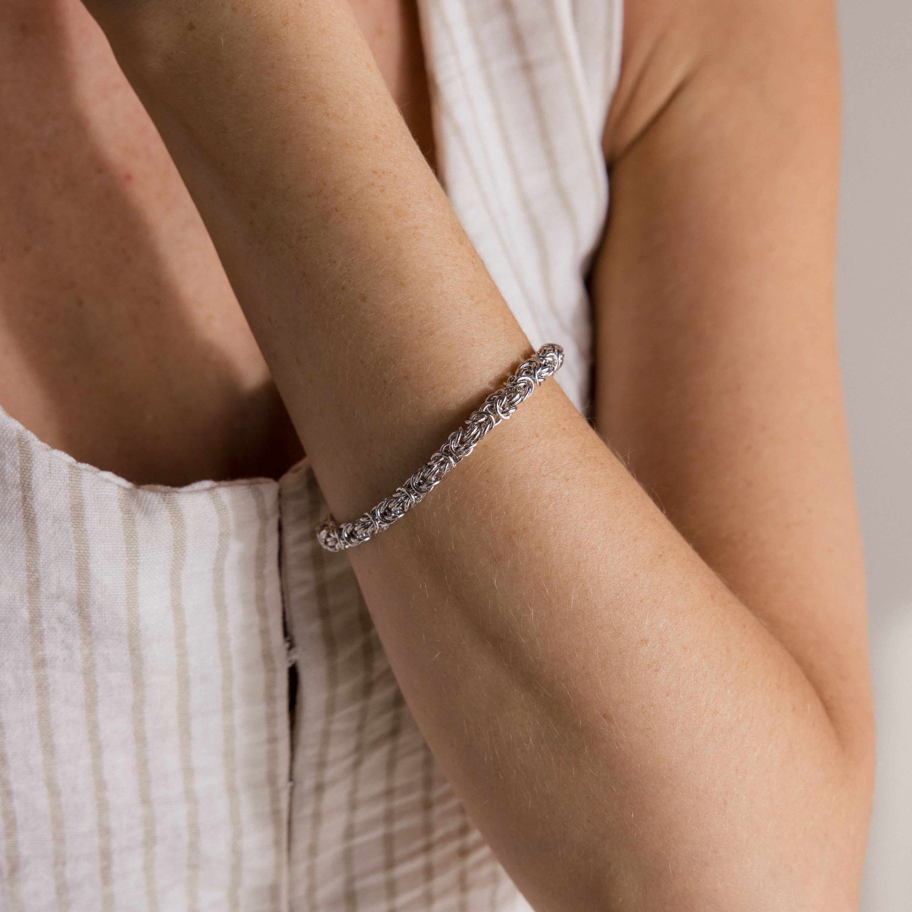 A person wearing a Bold Byzantine Bracelet and a sleeveless, white, striped top.