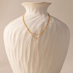 The Duo Satellite Lariat Necklace, featuring a minimal design and sparkling CZ diamonds, is displayed on a textured white ceramic vase against a neutral background.
