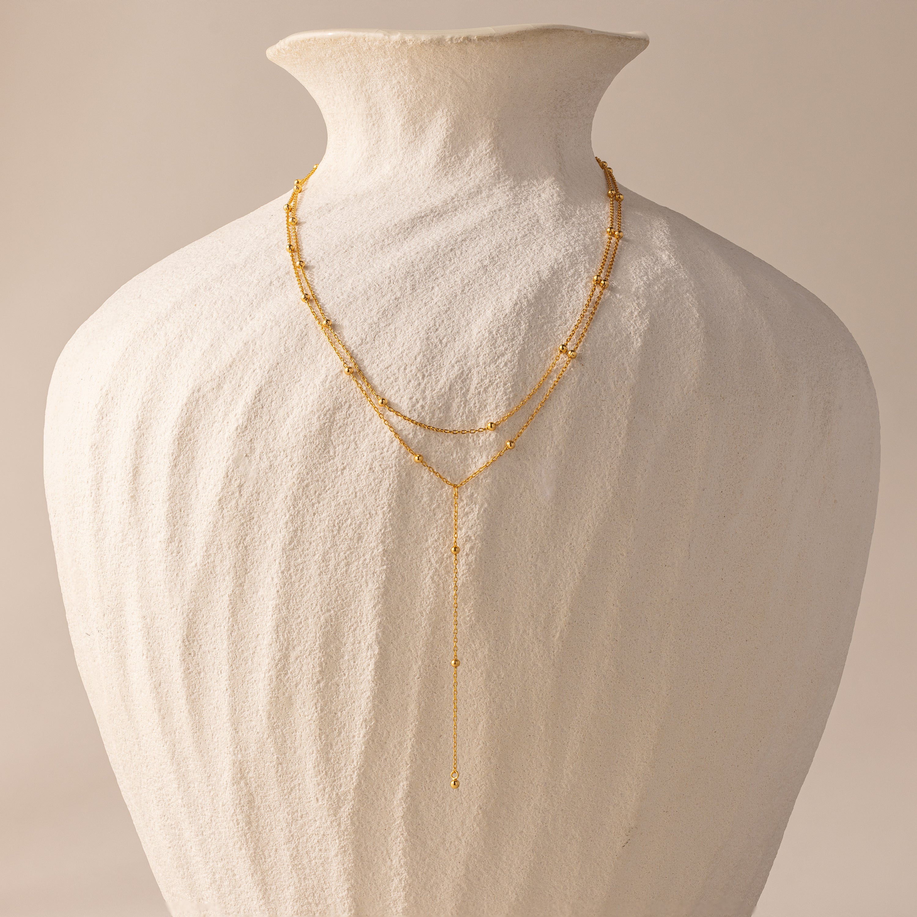 The Duo Satellite Lariat Necklace, featuring a minimal design and sparkling CZ diamonds, is displayed on a textured white ceramic vase against a neutral background.