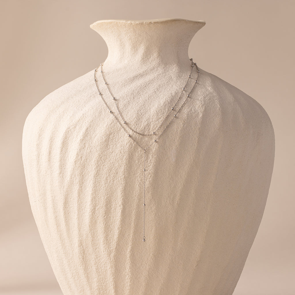 Duo Satellite Lariat Necklace draped over a textured white ceramic vase against a soft beige background—a minimal necklace sparkling with CZ diamonds.