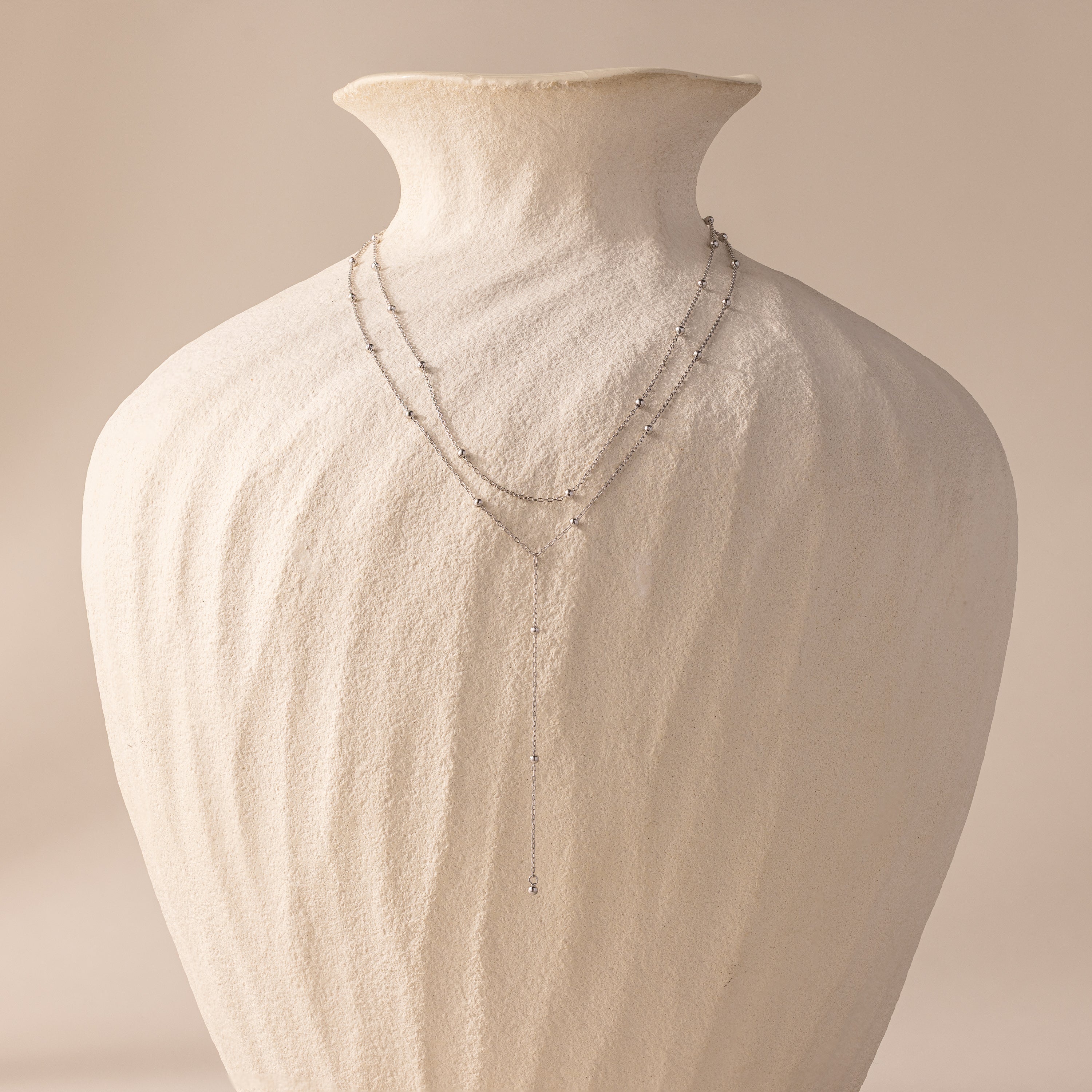 Duo Satellite Lariat Necklace draped over a textured white ceramic vase against a soft beige background—a minimal necklace sparkling with CZ diamonds.