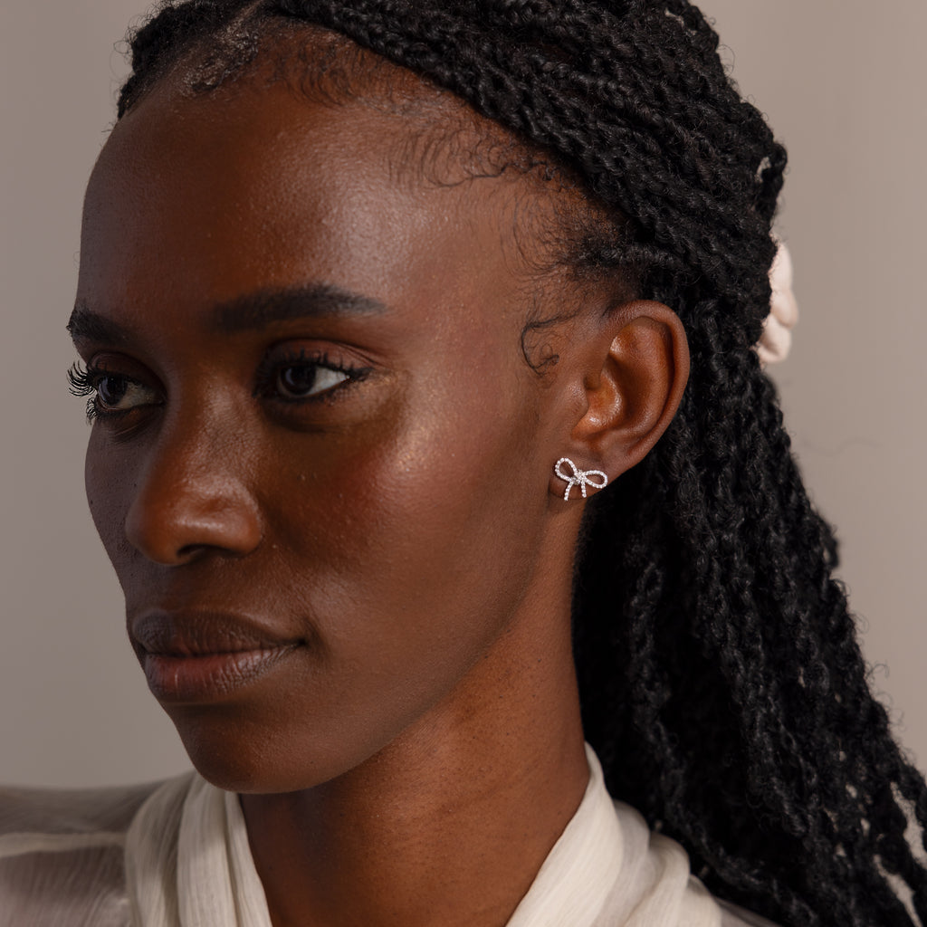 Model wearing silver bow-shaped stud earrings with sparkling stones, styled with a cream blouse for an elegant, refined look.