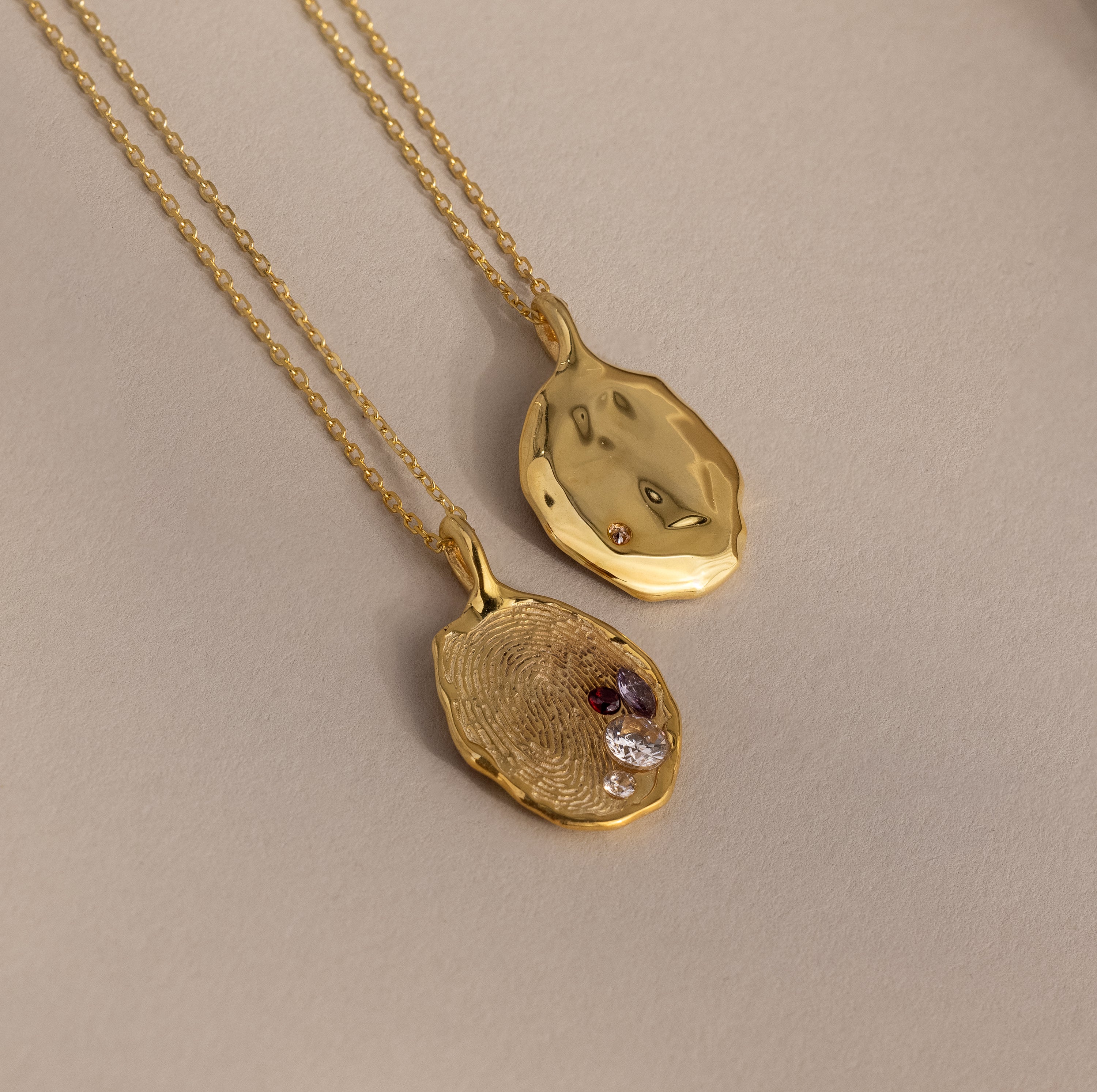 The Organic Fingerprint Multi Birthstone Necklace in 18K Gold, featuring colorful gemstone accents, is displayed on a neutral beige background.