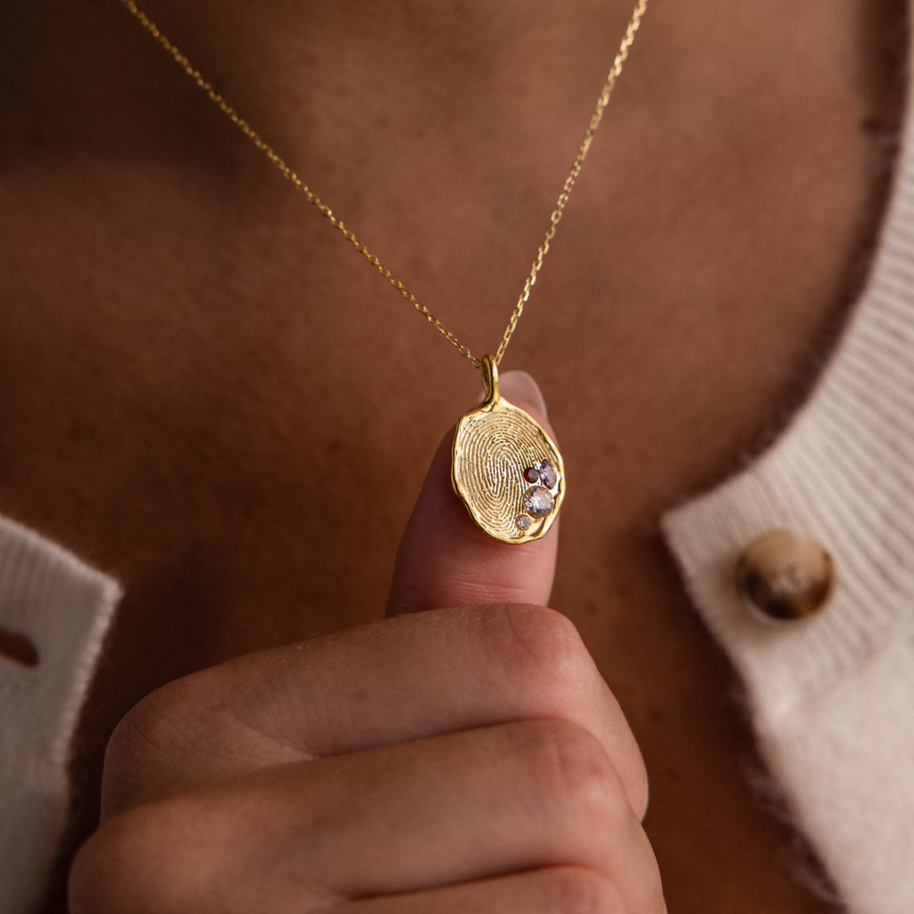 A person holds the Organic Fingerprint Multi Birthstone Necklace in Rose Gold close to their chest—a striking, personalized piece featuring unique fingerprints and sparkling birthstones.