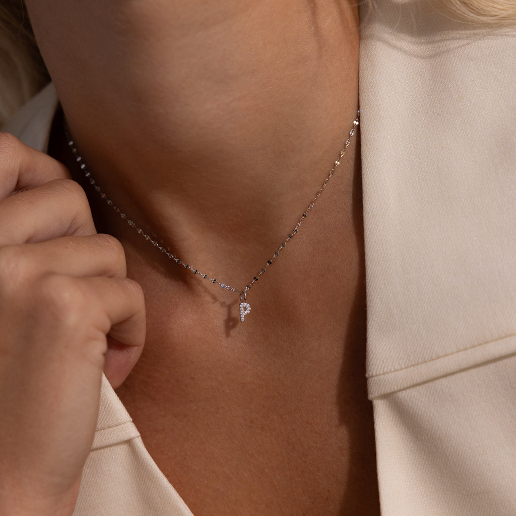 A person wearing a Dainty Pave Letter Necklace with a small pendant, styled with a cream-colored blazer.
