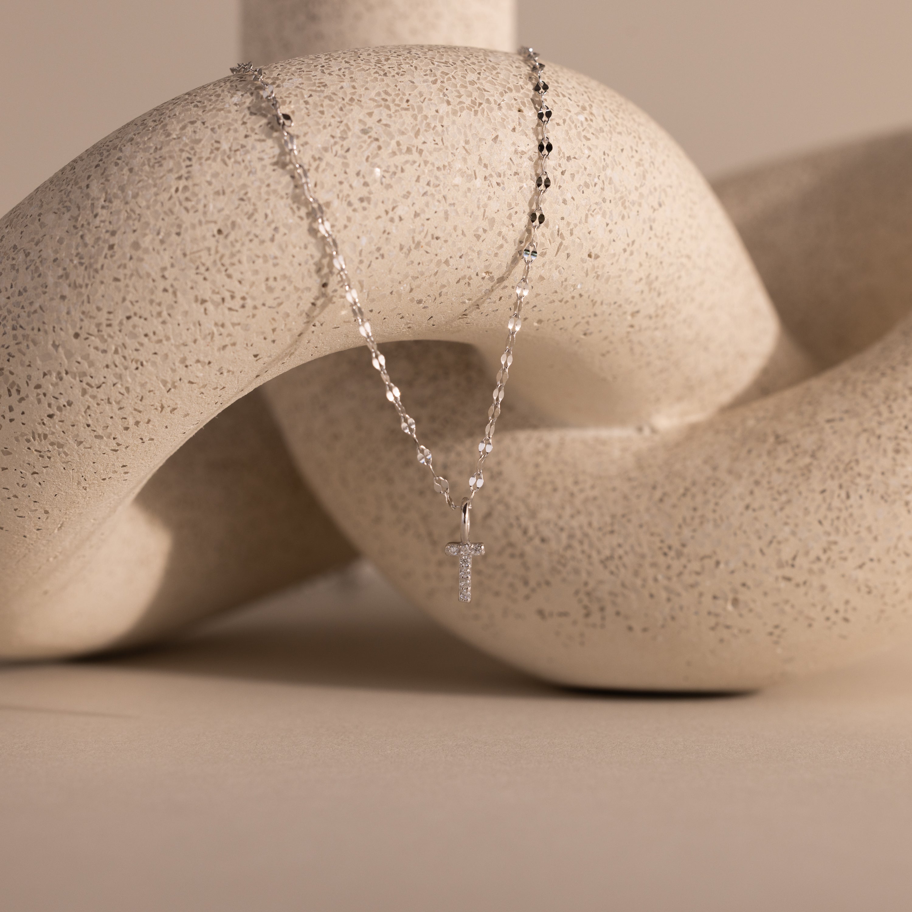 The Dainty Pave Letter Necklace in Sterling Silver is shown draped over a textured, curved beige sculpture.