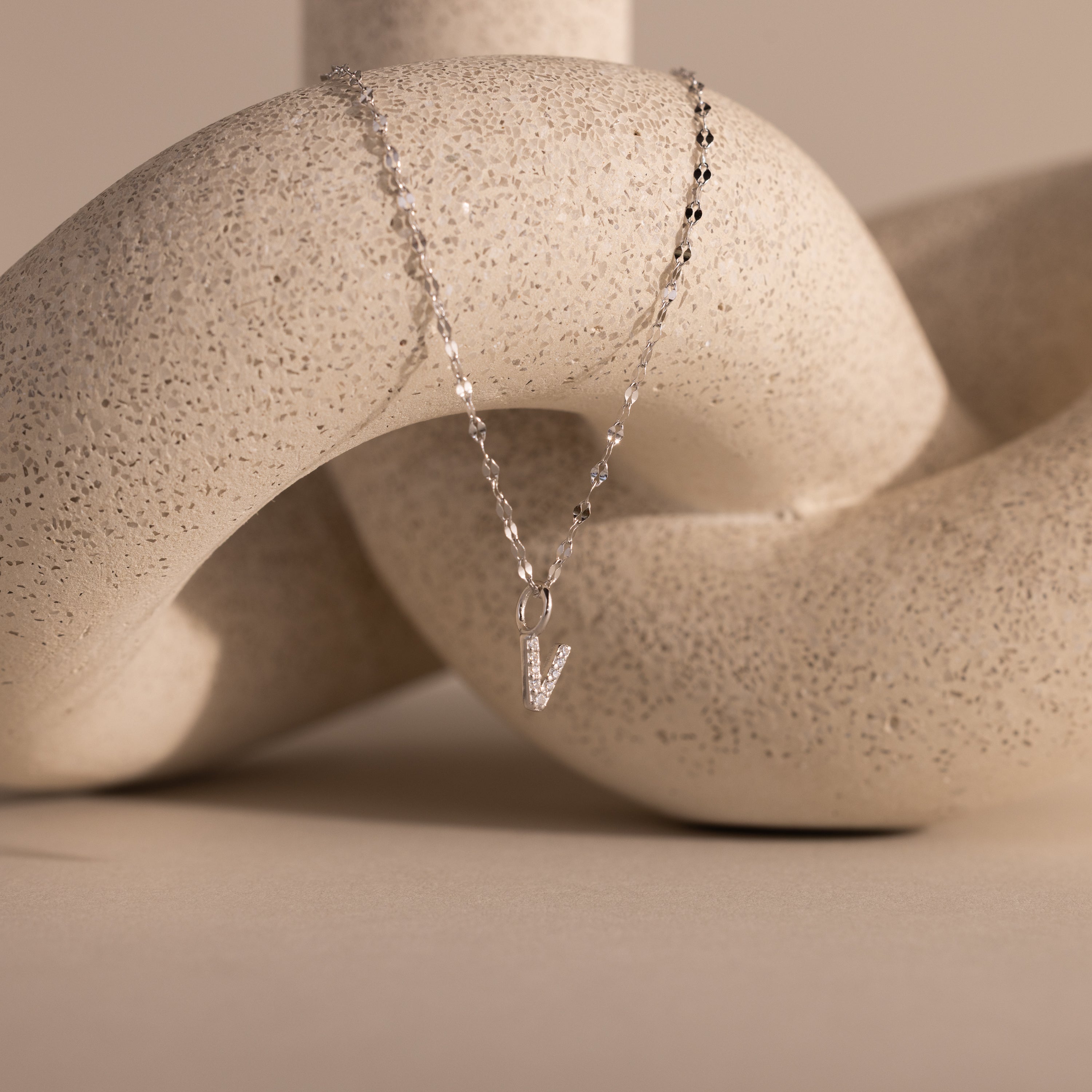 Dainty Pave Letter Necklace in Sterling Silver, displayed on a textured, abstract beige sculpture.