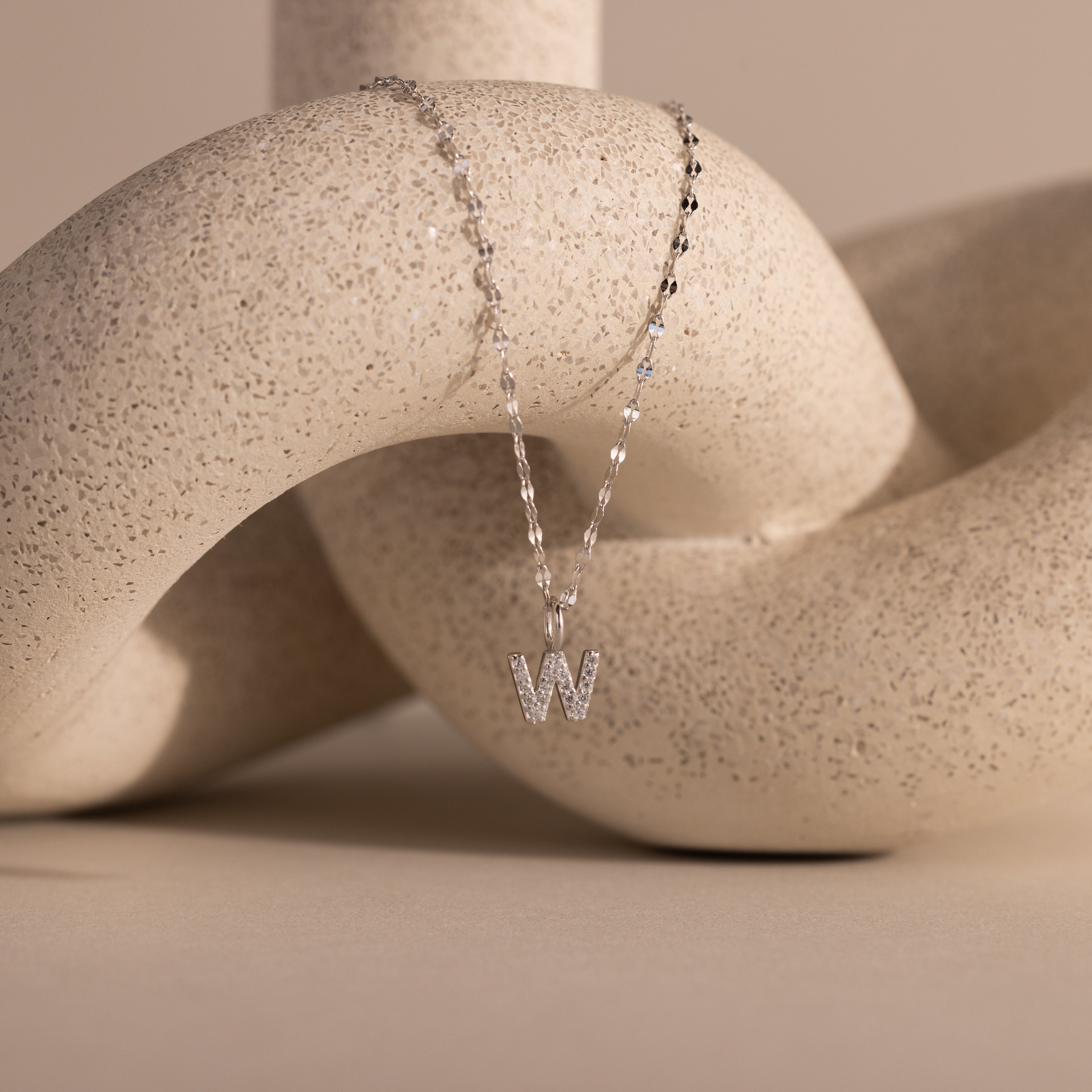 Dainty Pave Letter Necklace in Sterling Silver featuring a sparkling “W” pendant, elegantly displayed over a textured beige abstract sculpture.