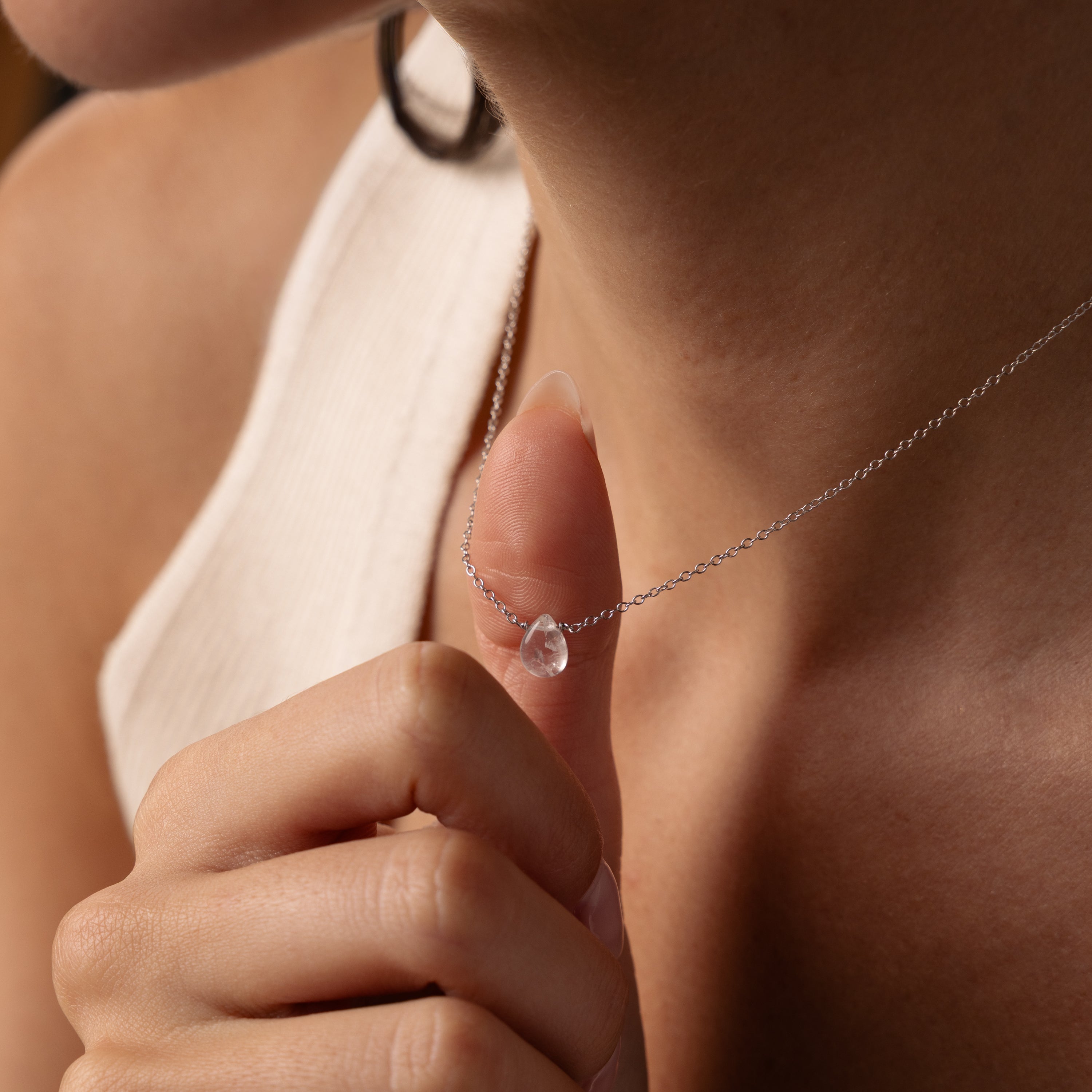 A person holds the Teardrop Moonstone Necklace near their neck, highlighting the refined elegance and minimalist design of this jewelry piece.