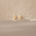 Moonstone Orbit Studs feature translucent moonstones and delicate crystal accents, exuding subtle elegance on textured beige paper. Perfect diamond-accent earrings for any occasion.