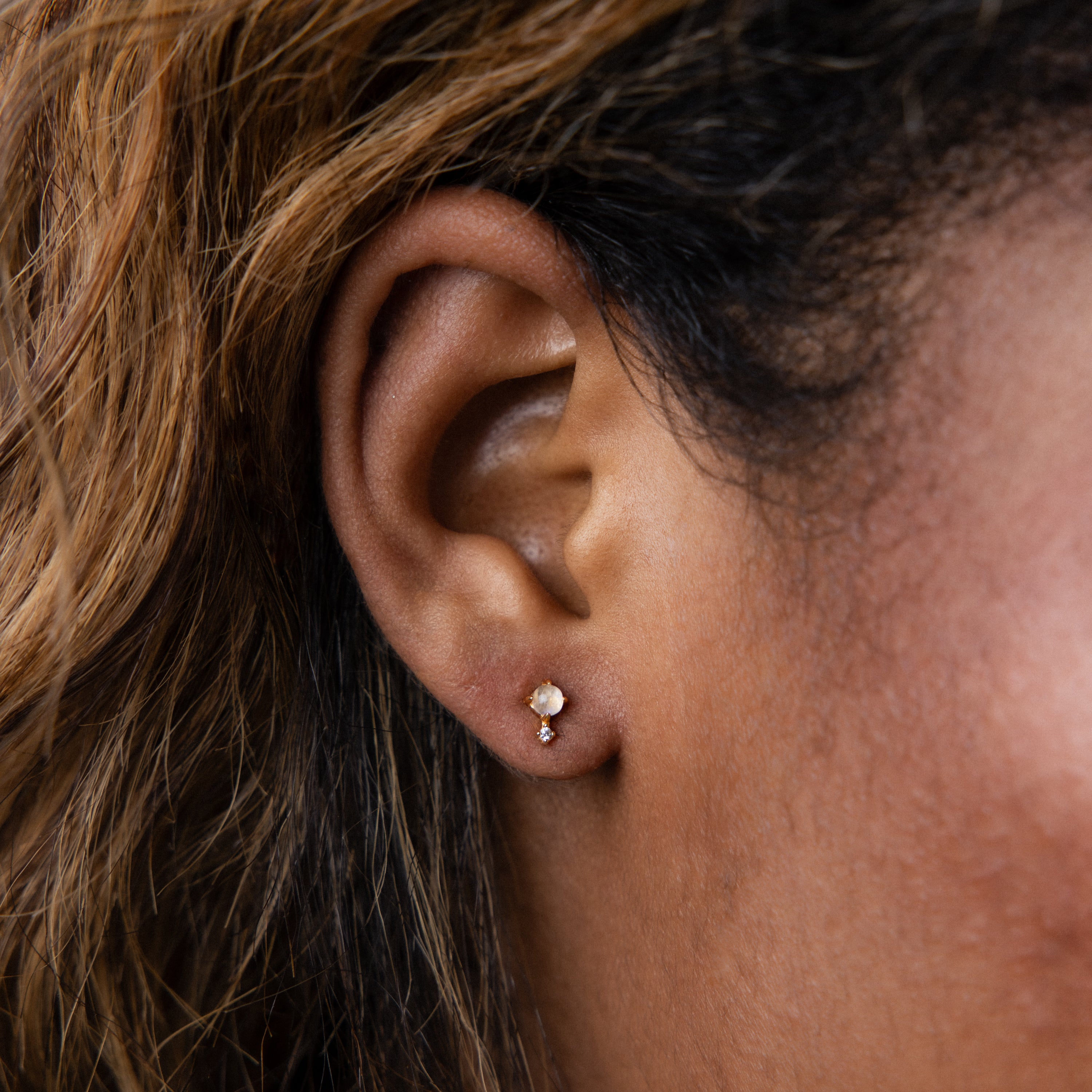 Close-up of a person’s ear wearing the Moonstone Orbit Studs in 18K Gold, delicate round earrings that combine elegant gold with moonstone.