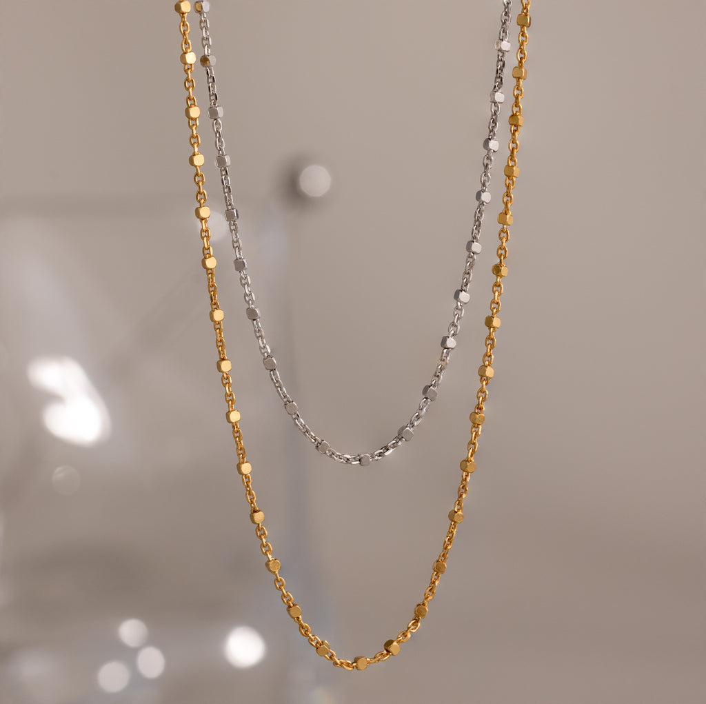 The Dot Station Necklace, available in silver and gold, is displayed against a neutral background—perfect for layering or wearing alone as a minimalist accessory.