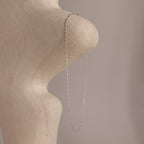 The Dot Station Necklace in Sterling Silver, featuring a delicate chain, is draped over a textured abstract beige sculpture set against a soft, neutral background.