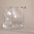 A delicate Dot Station Necklace in Sterling Silver is draped over a clear, wavy glass block with a silver rod on top, highlighting the minimalist piece’s refined elegance.
