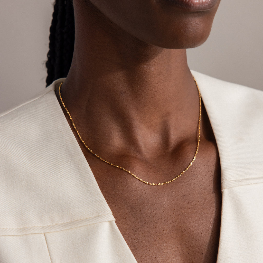 A woman in a cream-colored blazer completes her look with the Dot Station Necklace—a minimalist gold piece featuring simple dots on a delicate chain.