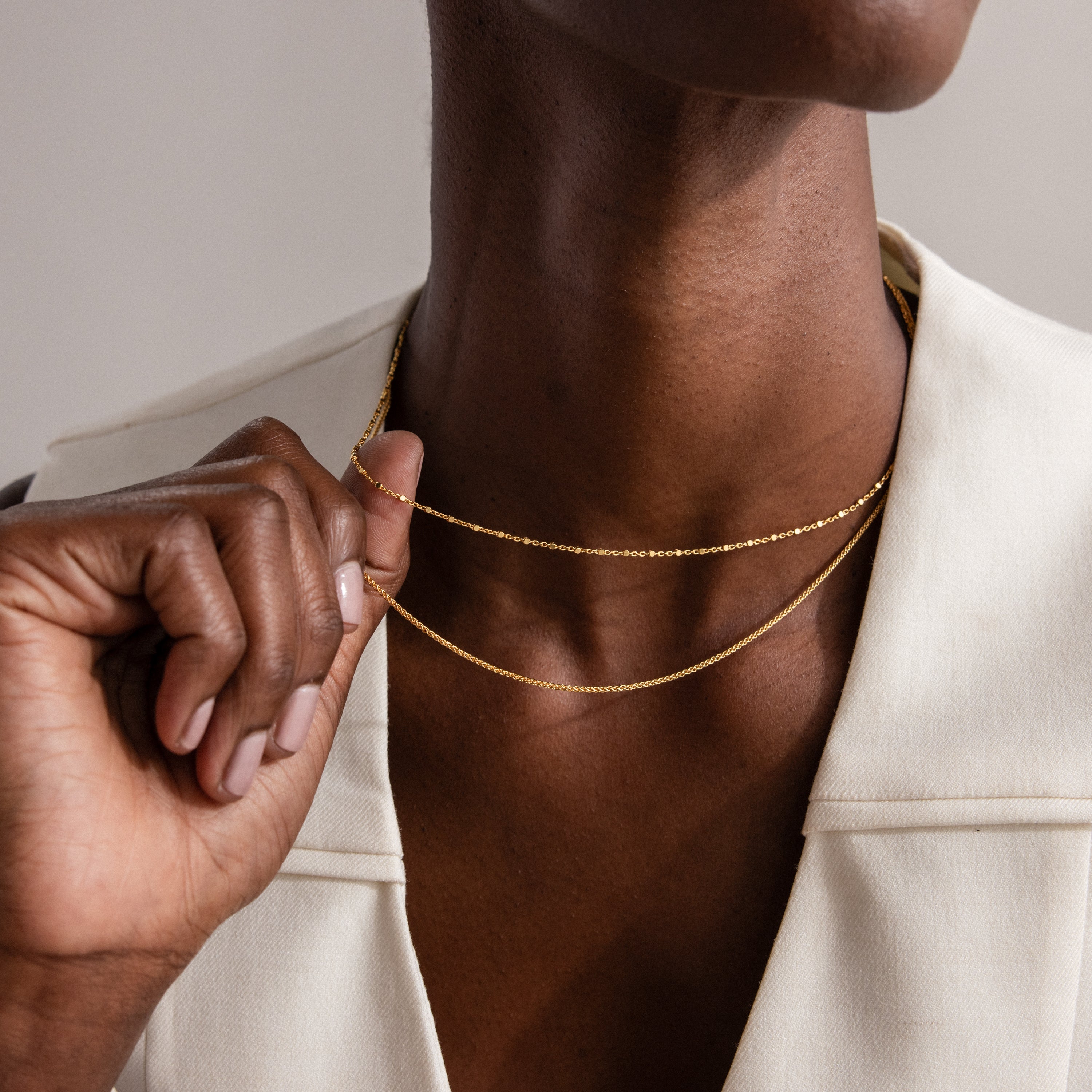 A person in a white blazer holds the Woven Chain Necklace in Sterling Silver—a sleek piece perfect for layering—against their neck.