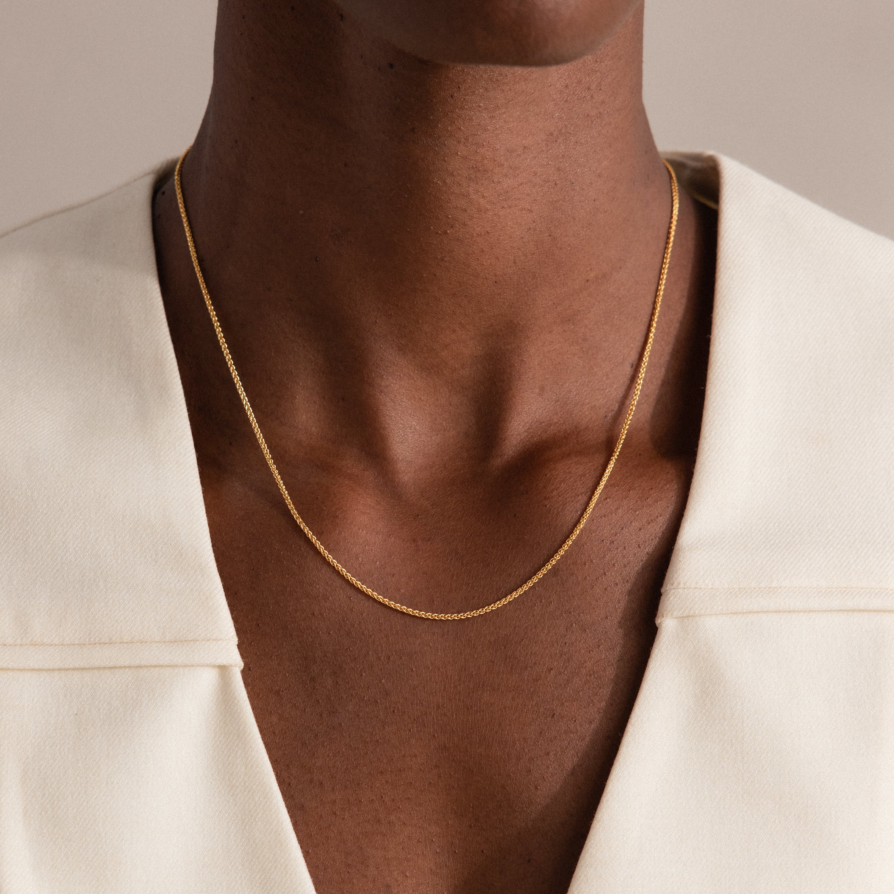 A person wearing the Woven Chain Necklace in 18K Gold paired with a cream-colored blazer.