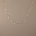 The Satellite Diamond Necklace in 18K Gold features small, evenly spaced clear crystal beads, displayed on a plain beige background.
