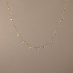 The Satellite Diamond Necklace in 18K Gold features small, evenly spaced clear crystal beads, displayed on a plain beige background.