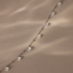 The Satellite Diamond Necklace in Silver, featuring evenly spaced round diamonds, rests on a textured beige surface bathed in soft light.