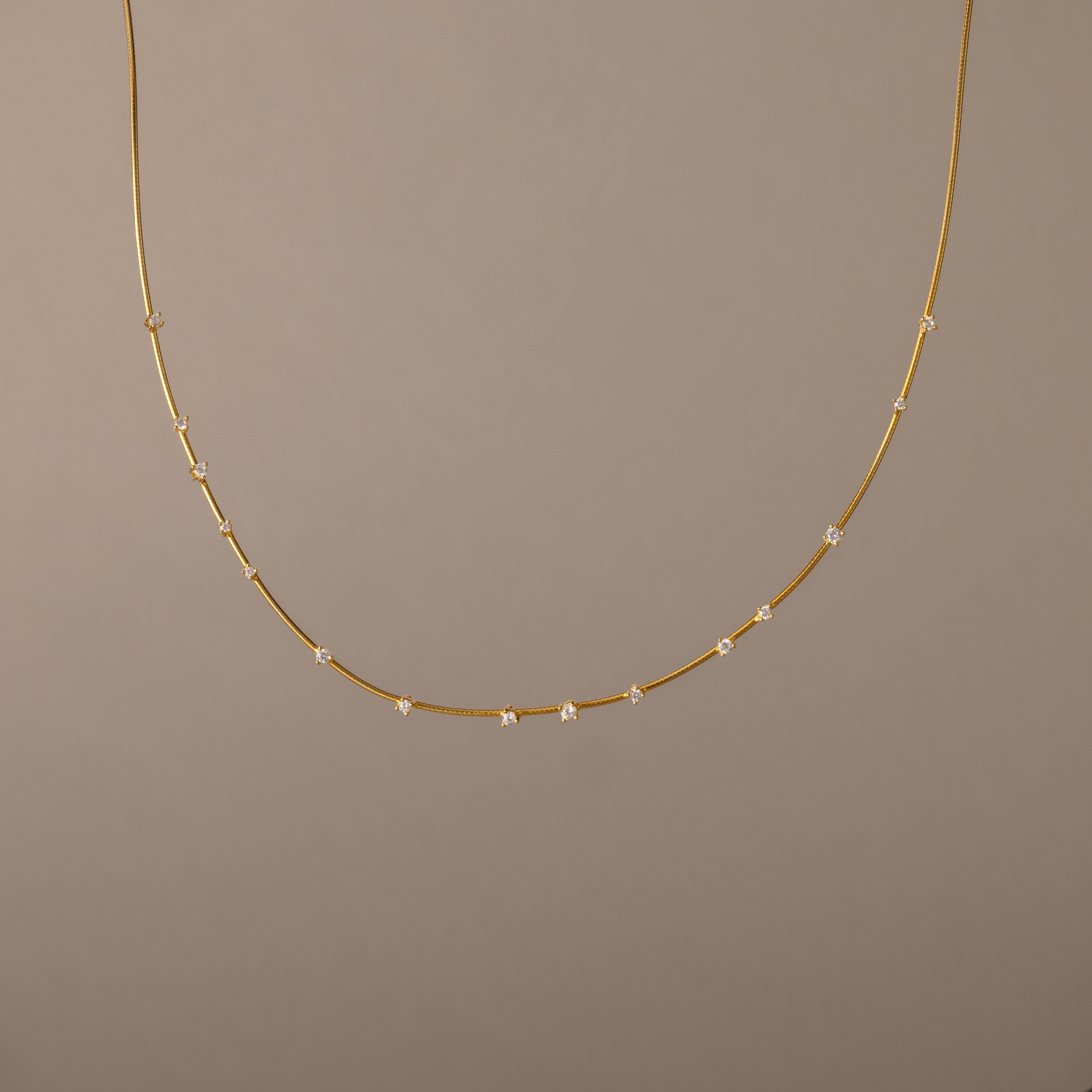The Sprinkle Diamond Necklace in 18K Gold features a delicate chain adorned with small, evenly spaced diamonds, shown against a plain beige background.