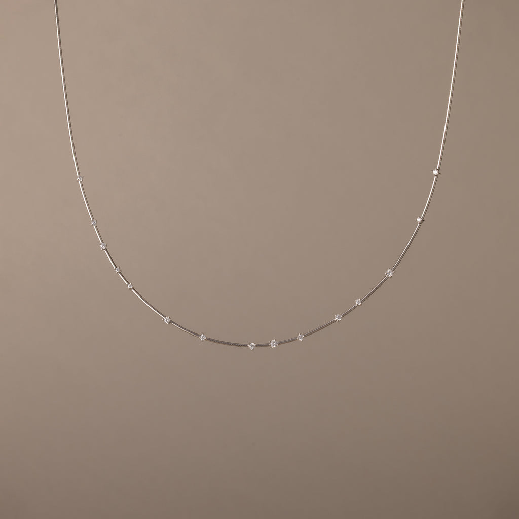The Sprinkle Diamond Necklace in Silver, featuring delicate, evenly spaced beads, is displayed against a plain beige background.