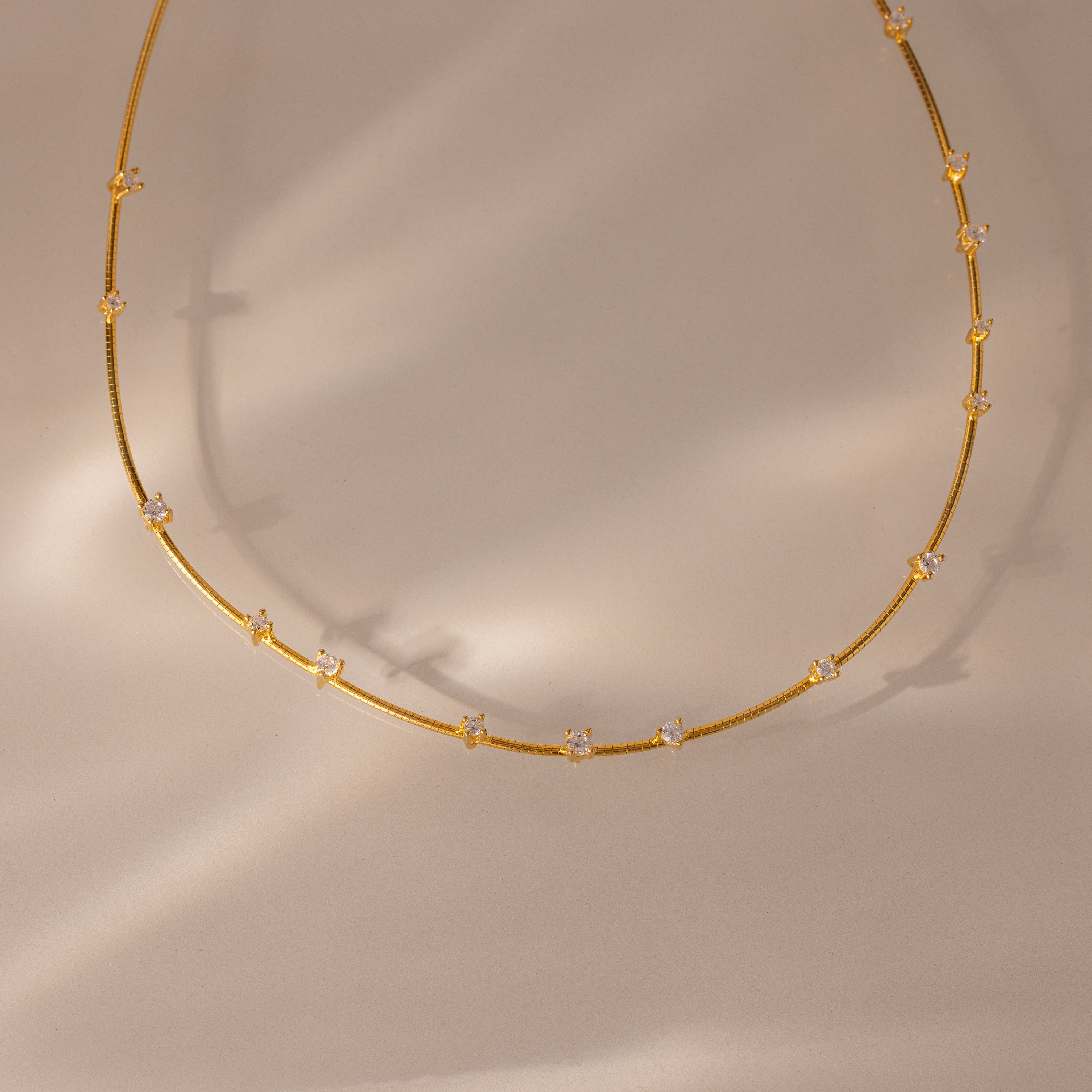 The Sprinkle Diamond Necklace in 18K Gold features delicate gold layering and small, evenly spaced diamonds, showcased on a neutral beige background.