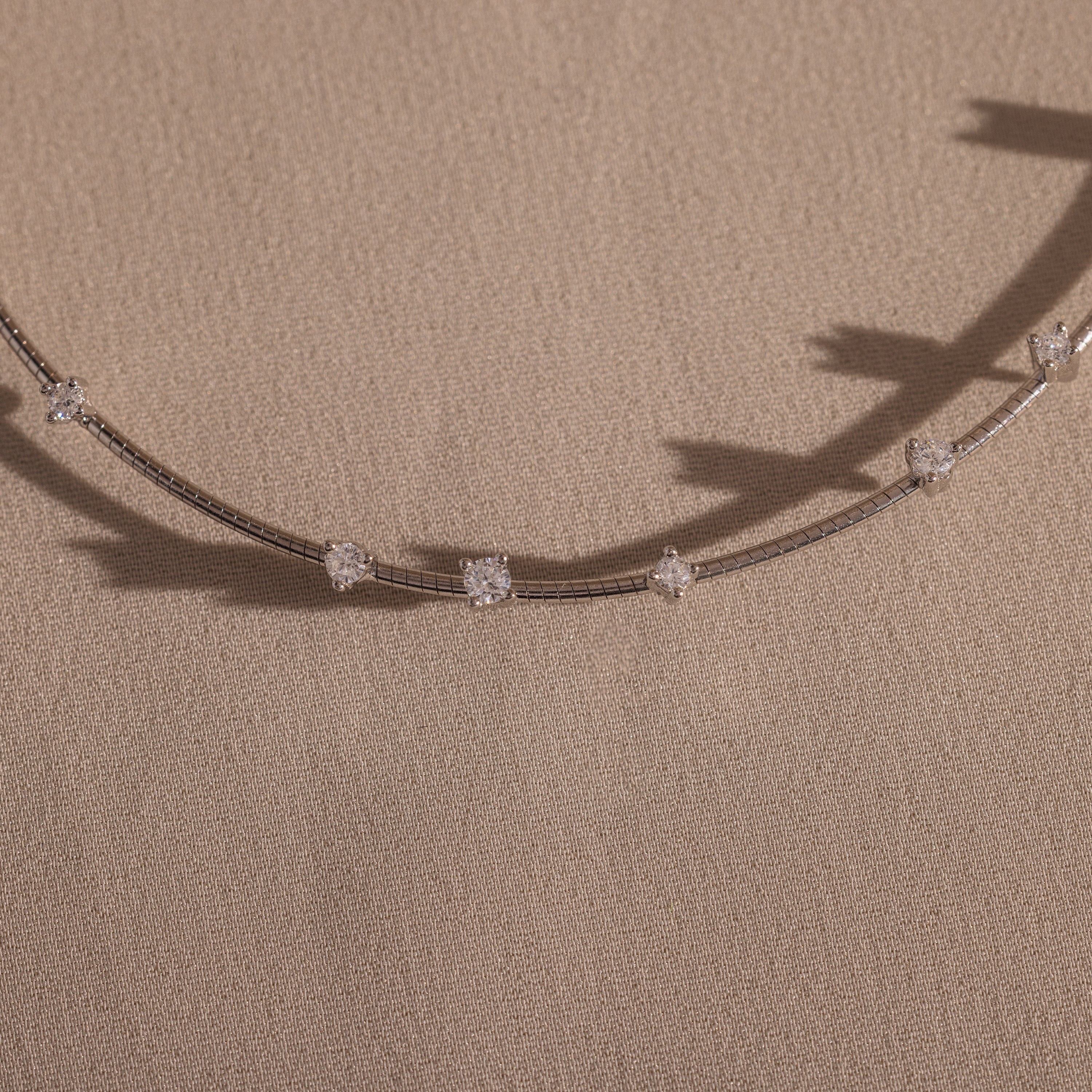 The Sprinkle Diamond Necklace features a delicate chain with evenly spaced clear gemstones, bringing everyday brilliance. Beautifully displayed on beige fabric.