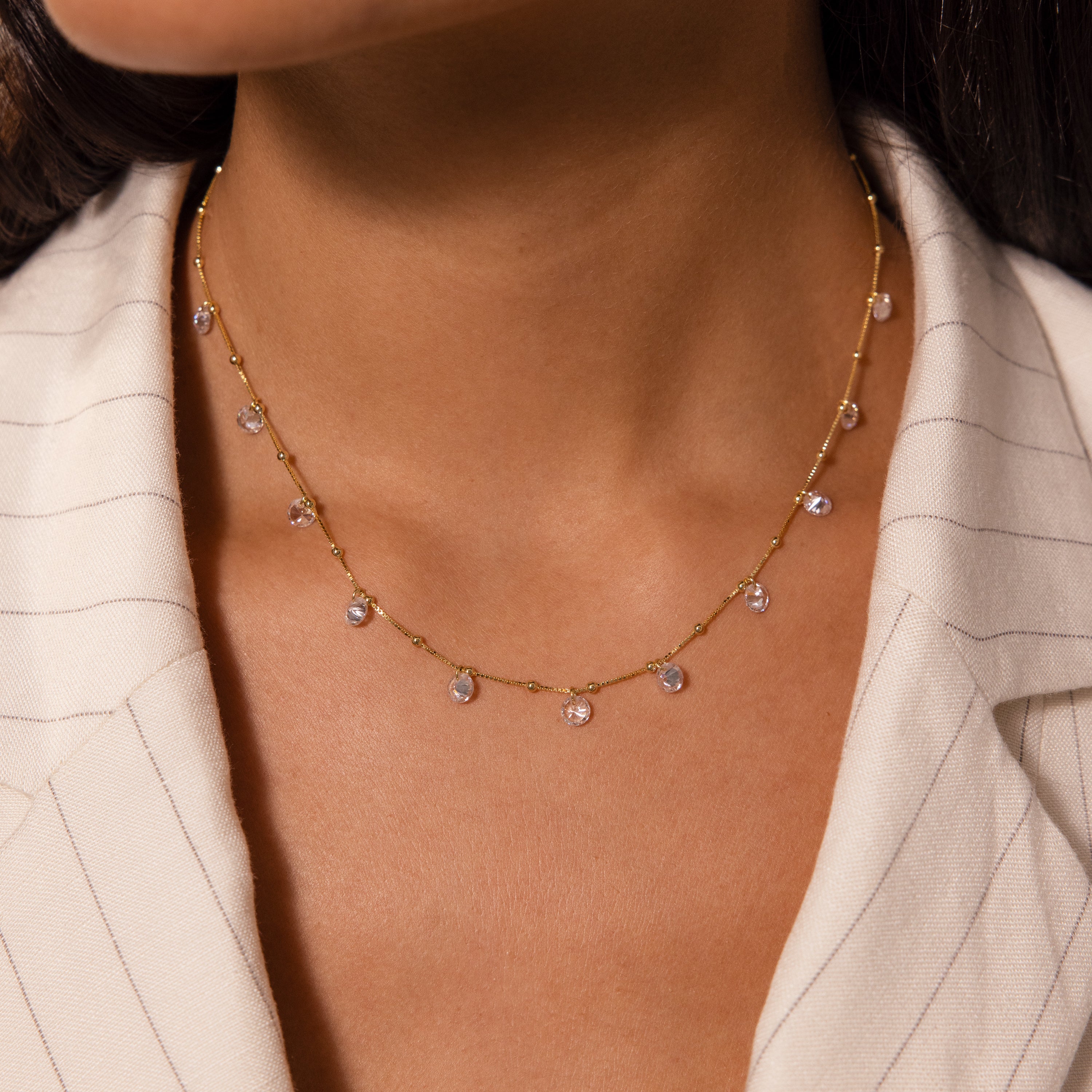 A woman wears the Satellite Diamond Necklace in 18K Gold, paired with a cream pinstripe blazer.