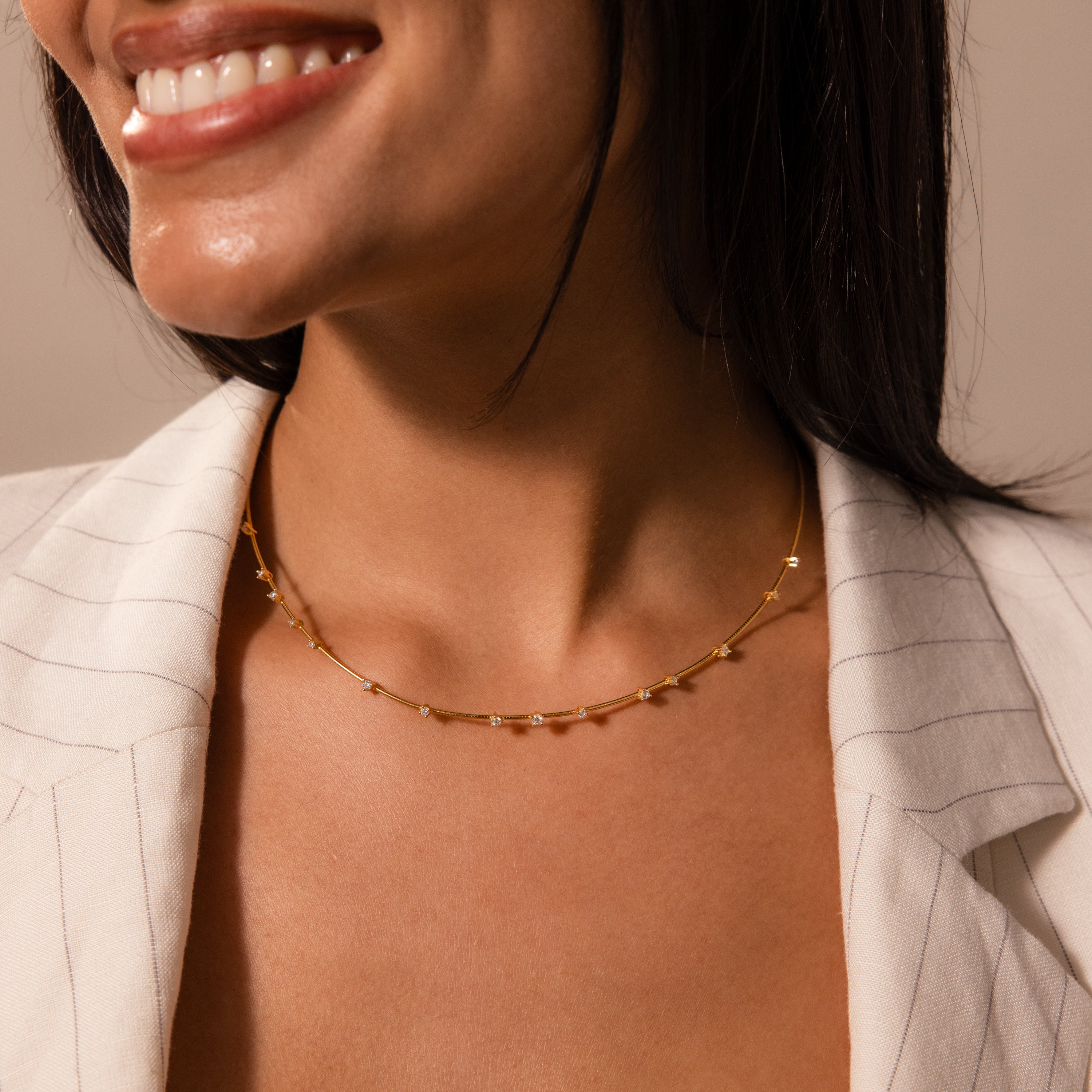 A woman wearing the Sprinkle Diamond Necklace with a delicate chain and a light pinstriped blazer smiles softly—an effortless touch of brilliance for every day.