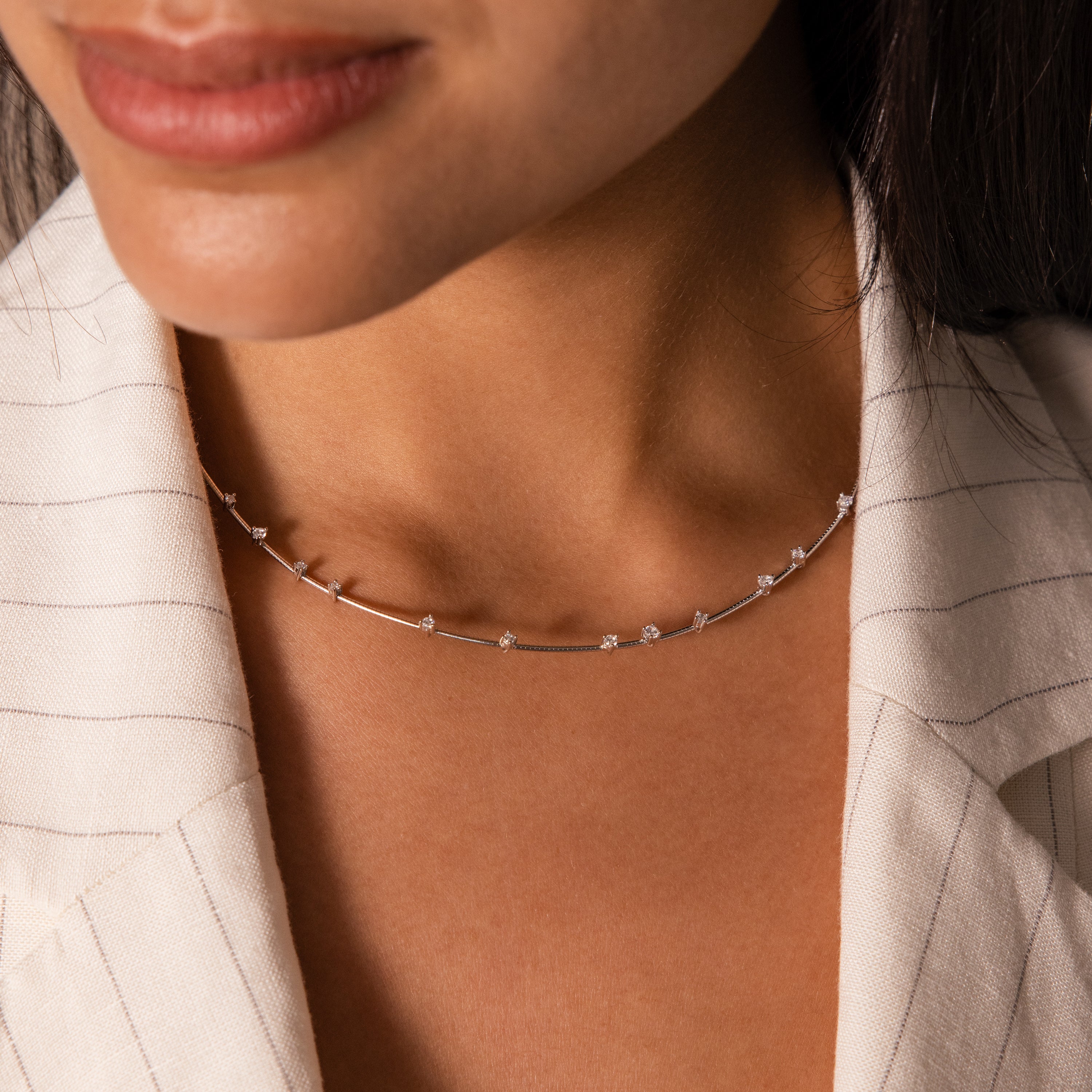 A woman wearing the Sprinkle Diamond Necklace in Silver, featuring delicate small gems, paired with a light pinstriped blazer.